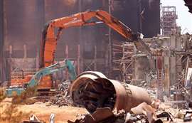 An excavator with shear attachments tearing down parts of the refinery structure