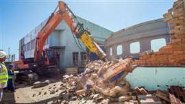 An excavator with a hydraulic hammerl attachment demolishes the wall of a tropical tank enclosure