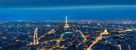 Aerial view of Paris by night with the Eiffel Tower in the centre of the shot, in the distance.