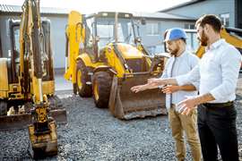Picture shows two construction professionals discussing in front of construction equipment. (Image: Adobe Stock image)