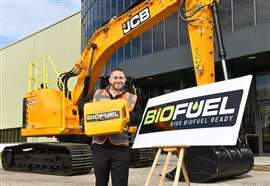 Un homme près d'une pelleteuse JCB jaune tenant un bidon de biocarburant à côté d'un panneau indiquant :