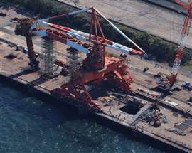 Vista aérea de una gran grúa de descarga de barcos roja y blanca en JFE Steel en Kawasaki, Japón, con el contrapeso faltante y un gran agujero en el muelle donde se hundió.
