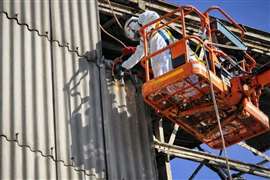 Person in hazmat suit on lift removing asbestos cladding