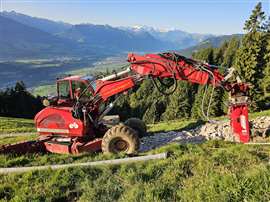 Excavotr al lavoro sul fianco di una montagna con vista sulle montagne svizzere sullo sfondo.