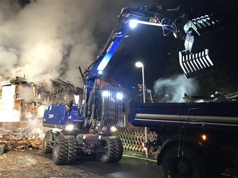 The Atlas 140W blue excavator loads parts of the roof onto a waiting truck.