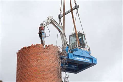The operator of the mini excavator, suspended from the all-terrain crane, at work on the chimney in 